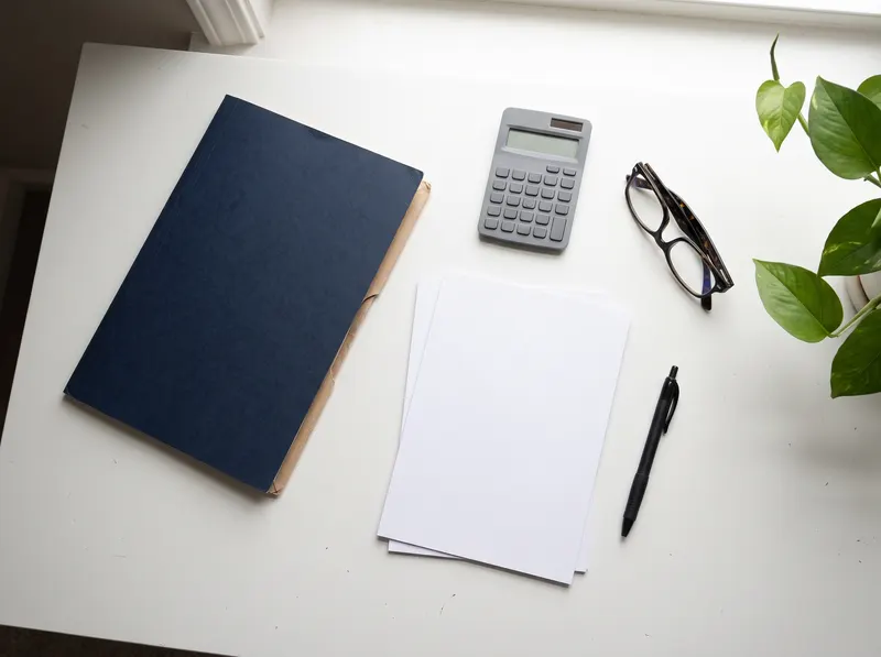 Schreibtisch mit Ordner, Taschenrechner und Brille